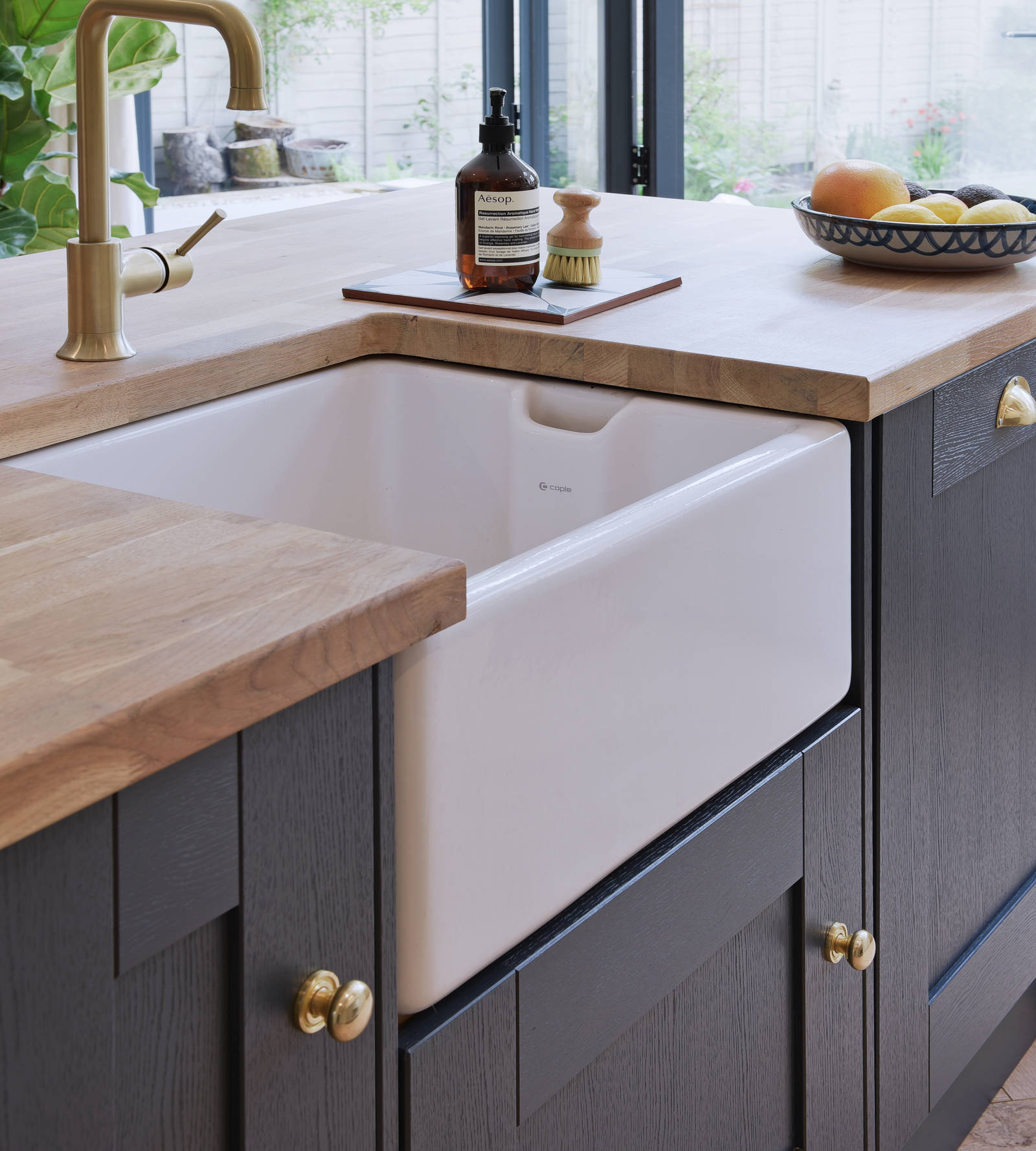 Close-up of Caple Belfast Ceramic sink which adds a rustic charm to the kitchen island. Paired with a wood worktop and brass tap.