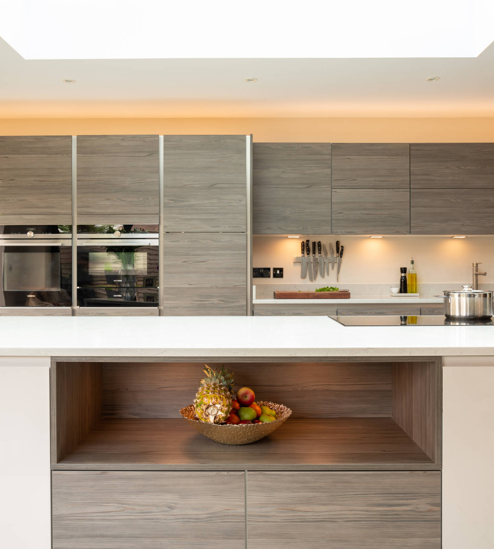 Close-up of kitchen island with low cabinets and an open shelf under the countertop, decorated with a fruit bowl
