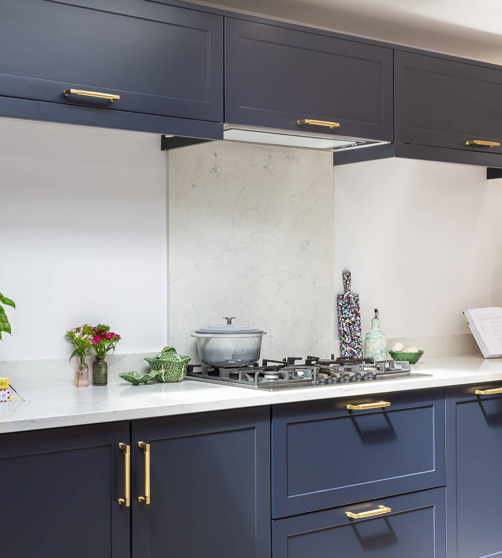 Dark blue shaker kitcen with top cabinets, integrated extractor, worktop matching the backsplash, gas hob and brass handles.
