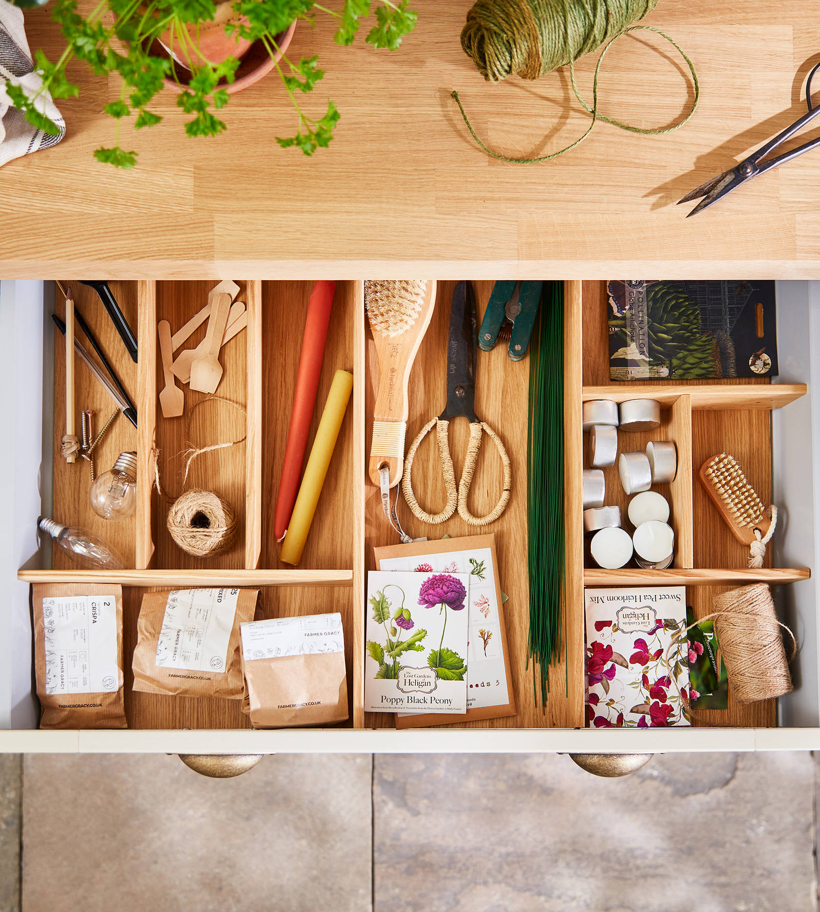 Overhead view of opened drawer in Winchester Sage utility room, with oak inserts sorting paper bags of seeds and other gardening tools.