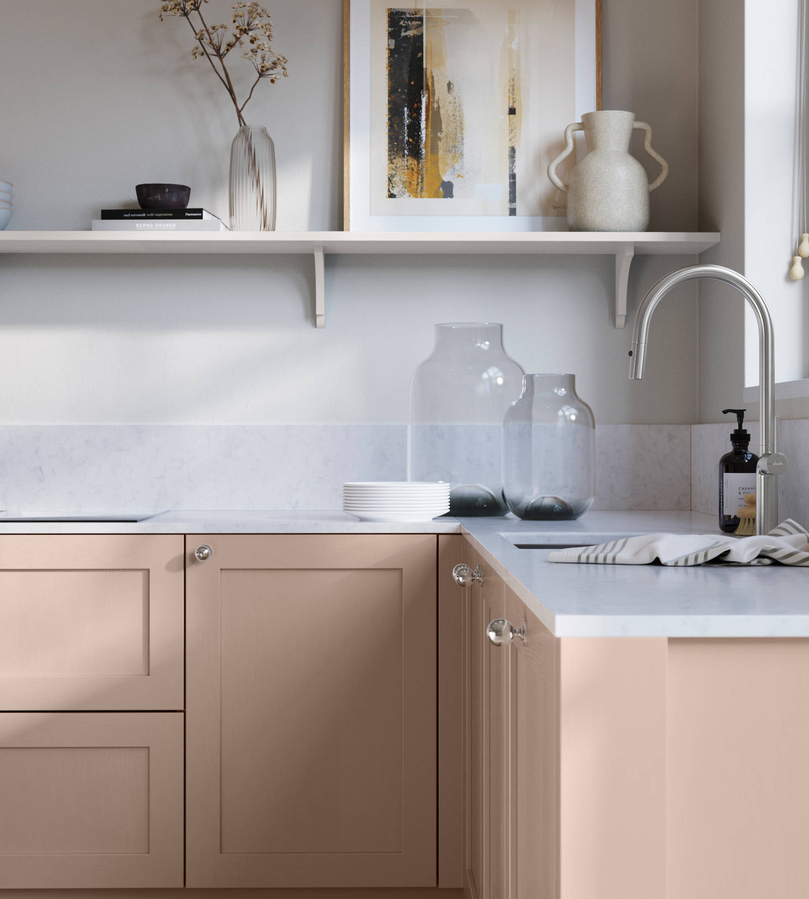Wardley Chalk Blush kitchen cabinetry with steel knobs, steel tap, white marbled worktop and matching backsplash. An open shelf on the wall above cabinets with ceramics and a vase of flowers.
