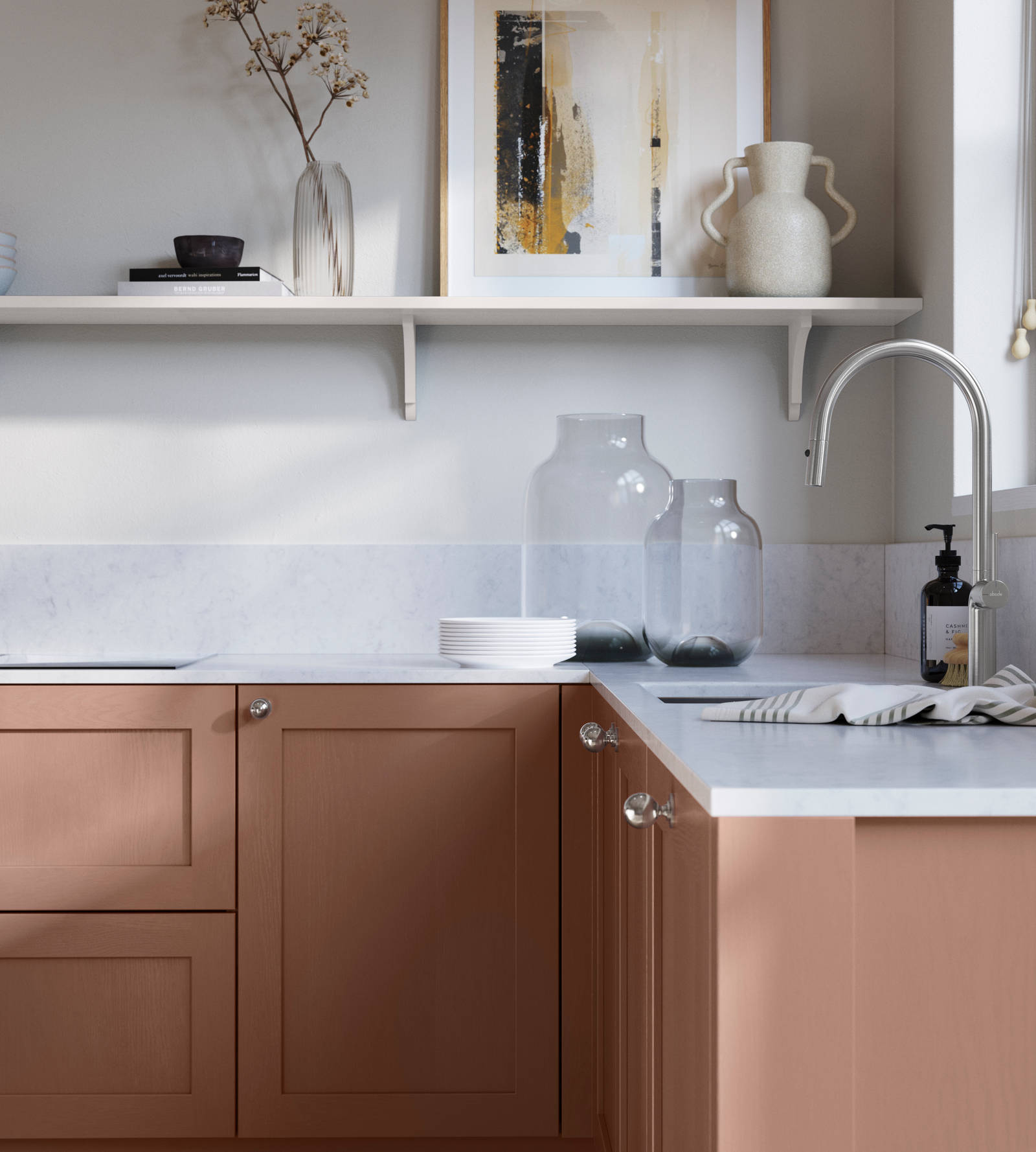 Wardley Clay kitchen cabinetry with steel knobs, steel tap, white marbled worktop and matching backsplash. An open shelf on the wall above cabinets with ceramics and a vase of flowers.