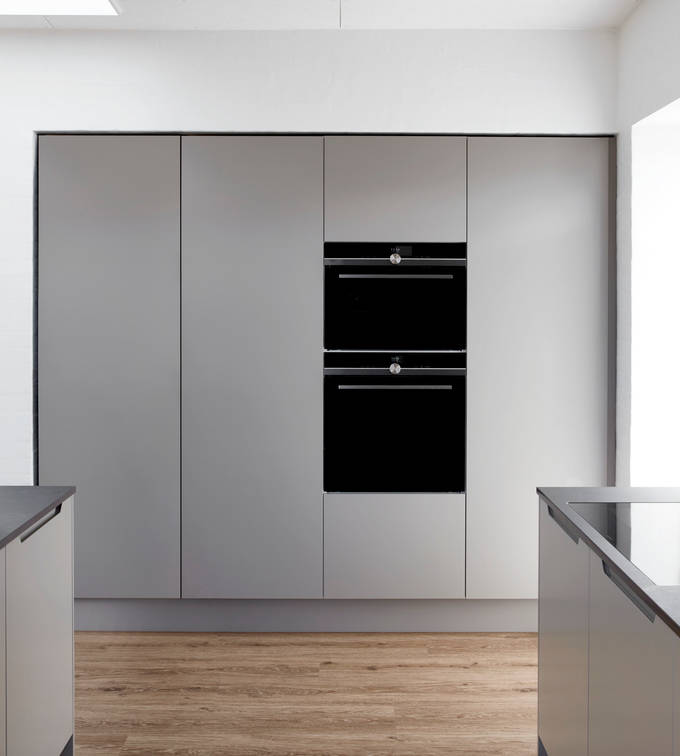 Højskabe med indbygningsovne i grå køkken Urban Søsten med køkkenø fra INVITA med indfræsede greb og sort bordplade