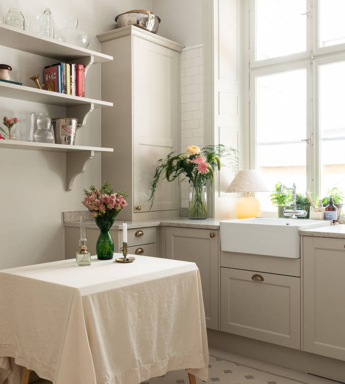 Sandra Beijers kök från Marbodal, Fagerö i den beige kulören Sand, med matchande öppna vägghyllor, en sittbänk med förvaring, diskho i porslin och handtag i mässing.