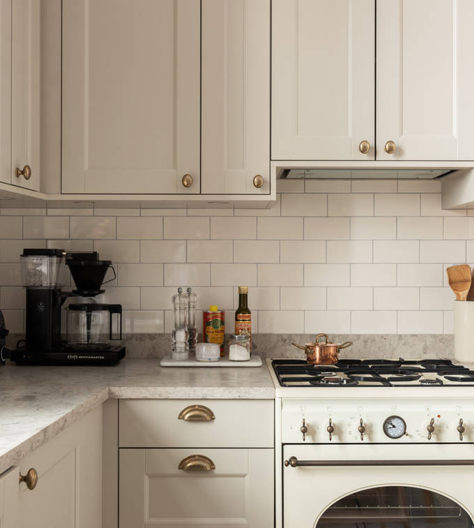 Sandra Beijers kök från Marbodal, Fagerö i den beige kulören Sand, med gasspis, vitt kakel som stänkskydd, och handtag i mässing.