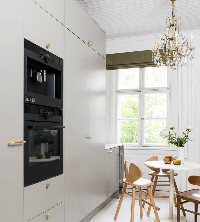 Tähkä Taupe sileämaalattu keittiö messinkinupeilla, sisäänrakennettu uuni ja kahvinkeitin korkeissa kaapeissa, pöytä puutuoleineen