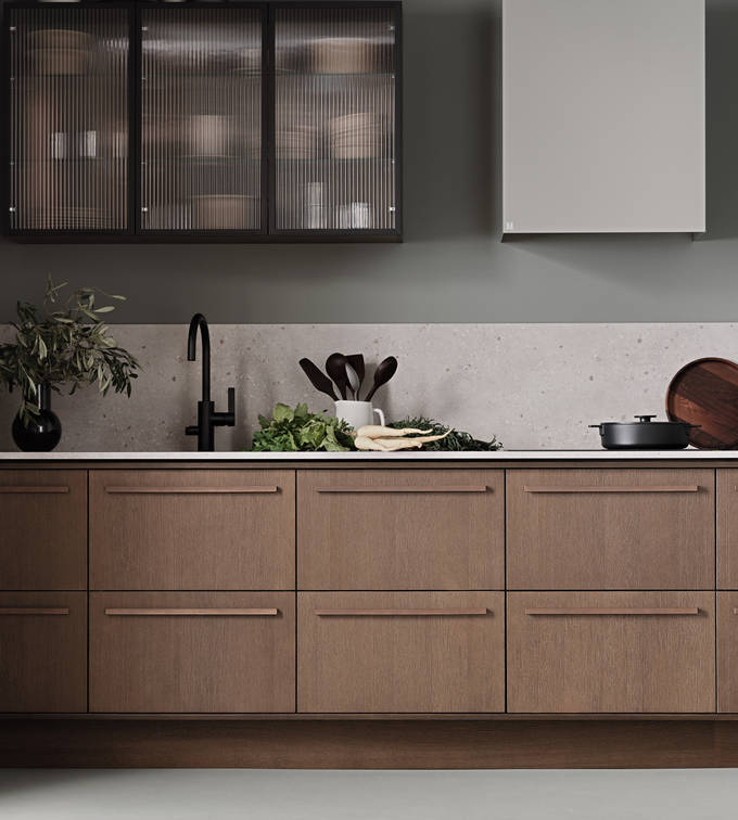 Køkken Forever Oak fra INVITA, mørk eg køkkenskabe med massiv tre mørk eg håndtag, komposit bordplade, sort armatur og vitrineskab med riflede glas i tynd, sort aluminiumsramme