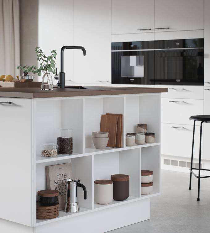 Hvit kjøkken og kjøkkenøy med slank og elegant front med svakt avrundede kanter, Corestoen varm sement benkeplate, sort kran, endehyller i kjøkkenøya.