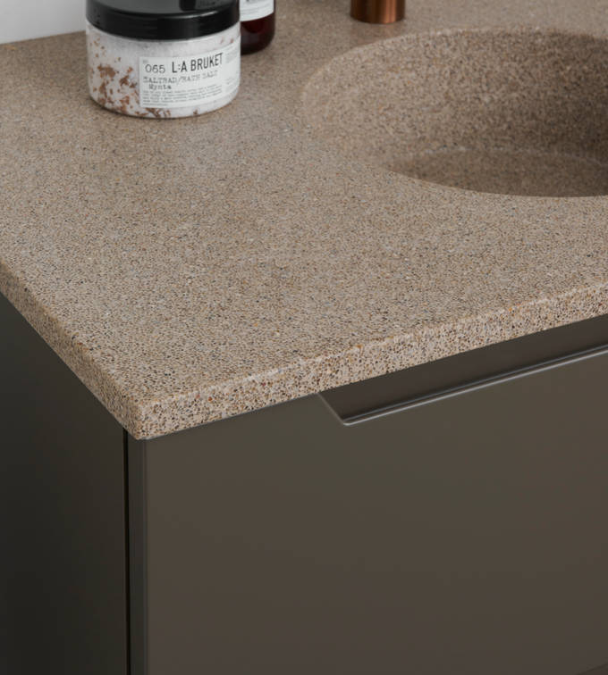 Nærbillede af bordplade stone beige 99 med vask cannes-30-30 og Cassøe borstet kobber armatur i moderne badeværelsesmøbel Urban med indfræsede greb i brune farve Bark og