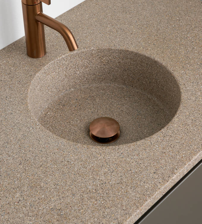 Nærbillede af bordplade stone beige 99 med vask cannes-30-30 og Cassøe borstet kobber armatur i moderne badeværelsesmøbel Urban med indfræsede greb i brune farve Bark og