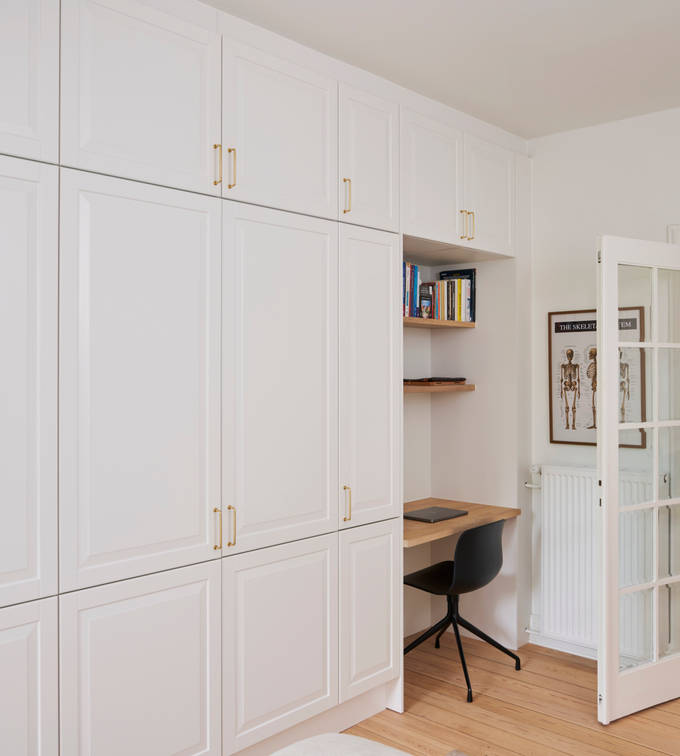 Hvid garderobe Nordic Frost fra INVITA med fyldningslåger og messinggreb, med indbygget bordplade med stol og væghylder til hjemmekontoret