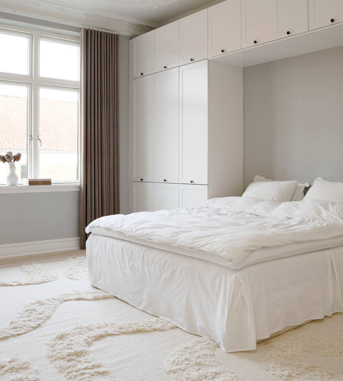 Hvid tidløs garderobe Square Sand fra INVITA omkring en seng med en kommode over, sorte greb på karmdøren