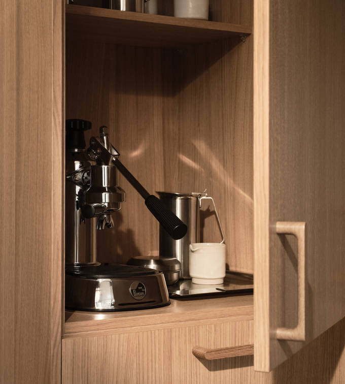 Öppnat skåp i Siri Barjes kök, ekskåp med kaffemaskin i skåpet, handtag i ek.