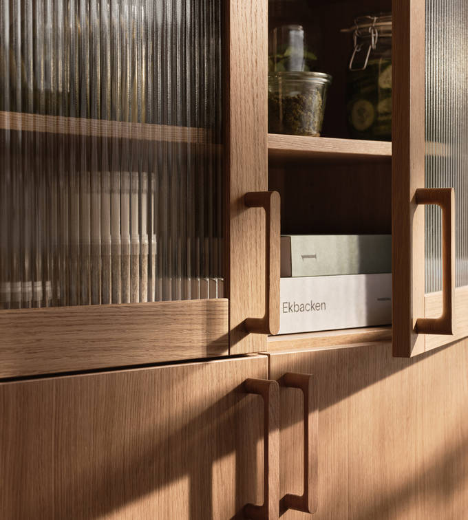 Öppnat vitrinskåp i Siri Barjes kök, räfflat glas i ram av ek, med matchande ekluckor på skåpen under och handtag i ek.