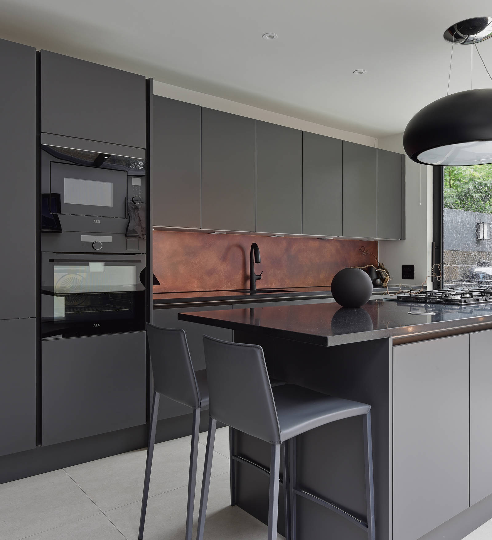 The monochrome, dark and decadent I-shaped Integra Soho Charcoals kitchen with a kitchen island, a Black granite worktop and integrated ovens in tall cabinetry.