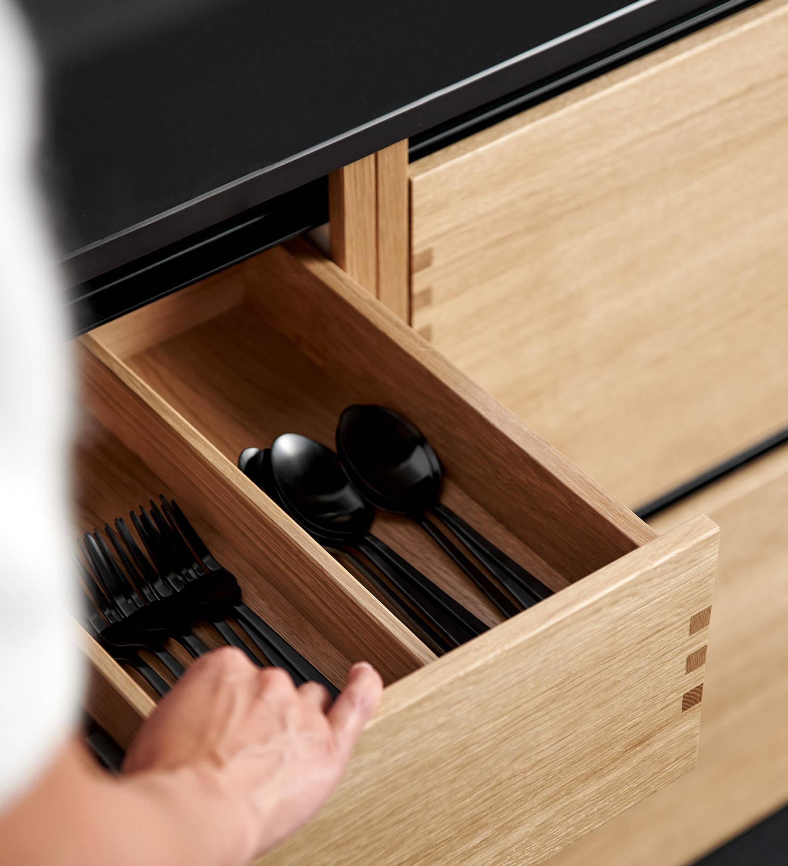 Nærbild av køkken Glød fra INVITA, åben bestikskuffe i massivt egetræ med fingertappede samlinger  og sort granit bordplade