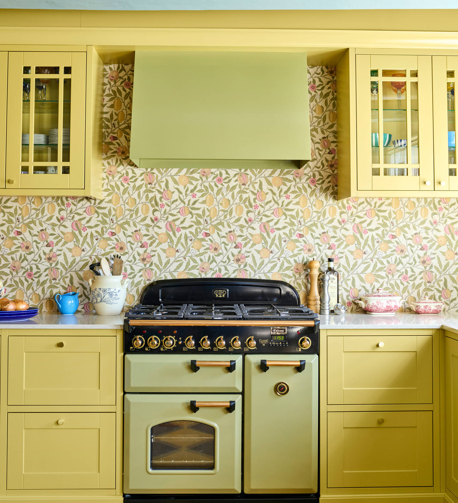 Landlig rammekjøkken Scala Inframe fra Sigdal som gir en snekkerbygged preg, vitrineskaber, Falcon Classic Olive green komfyr med gassbrennere og Røroshetta Grue ventilator i samma fargekode, rutete gulv