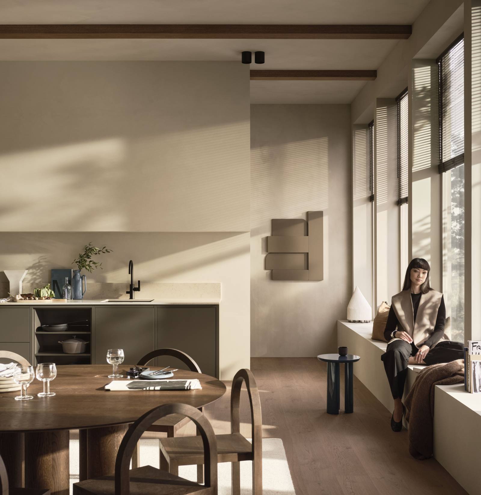 Ett stort rum i Warm Minimalism-stil med kök och en kvinna vid fönster.