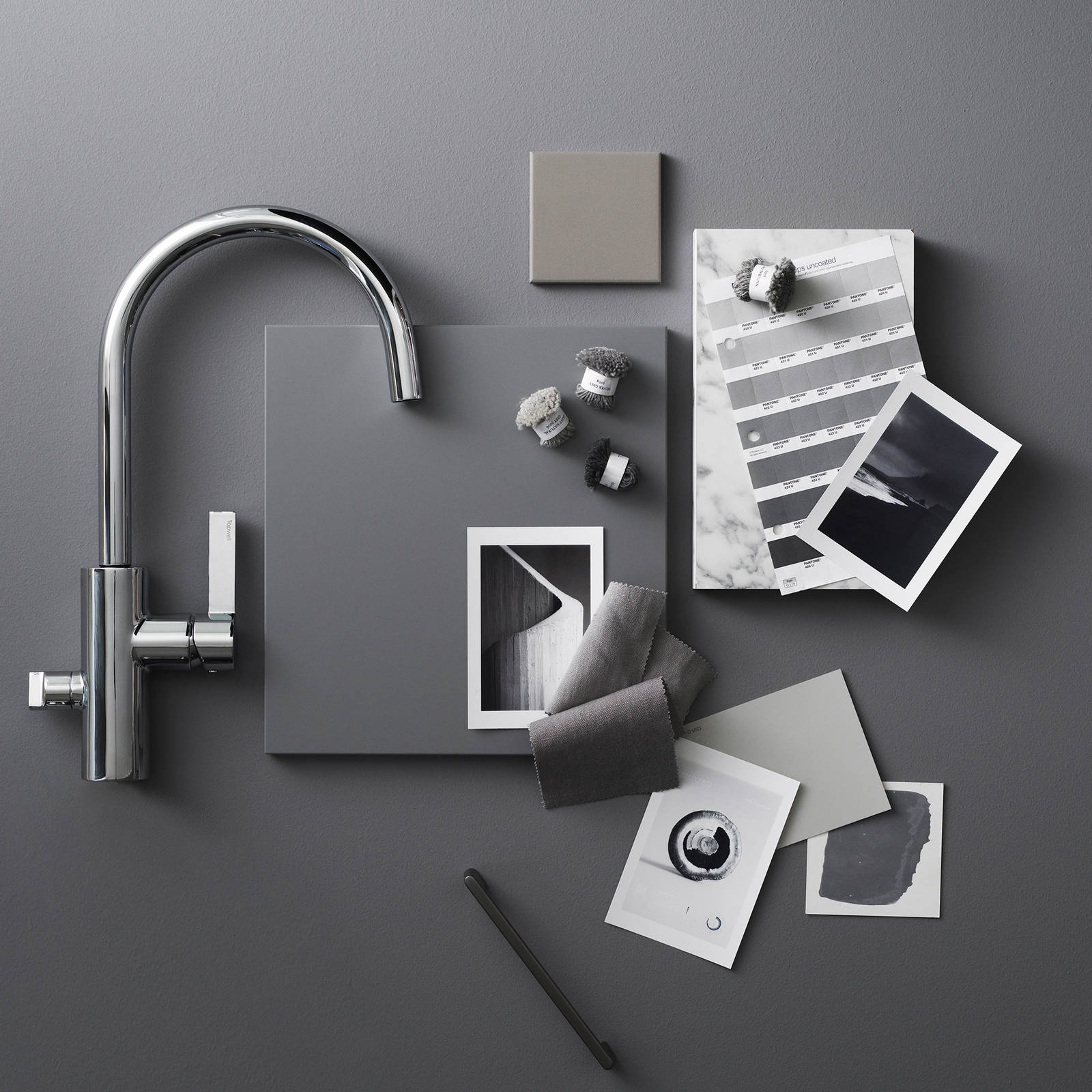 Moodboard med mörkgrå kökslucka, blandare i rostfritt stål, marmor, foton med svartvita motiv och ett svart handtag