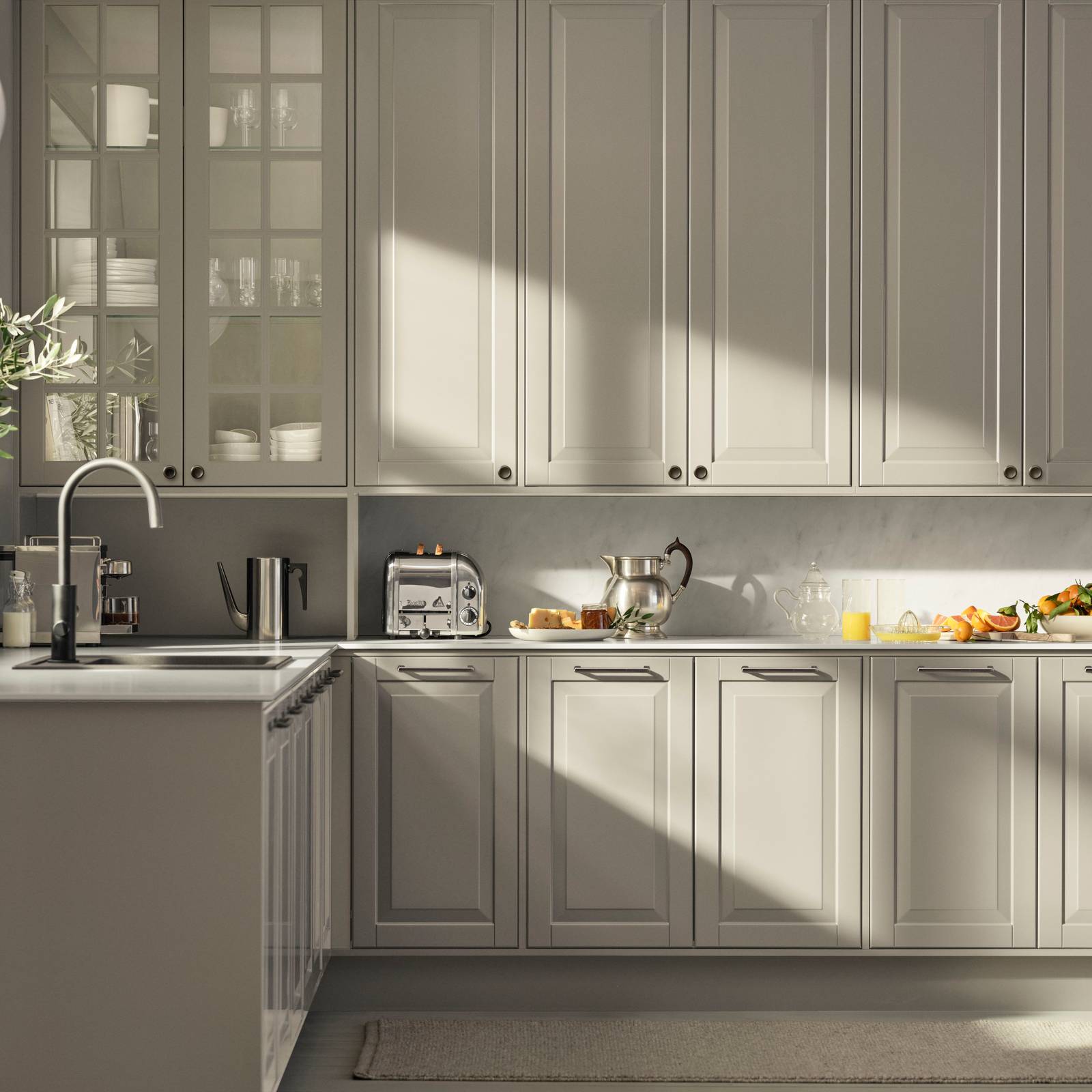 Beige landkøkken Nordic Sand fra INVITA med fyldningslåger, sort håndtag, vitrineskab med sprosselåger og hvid marmor laminatbordplade