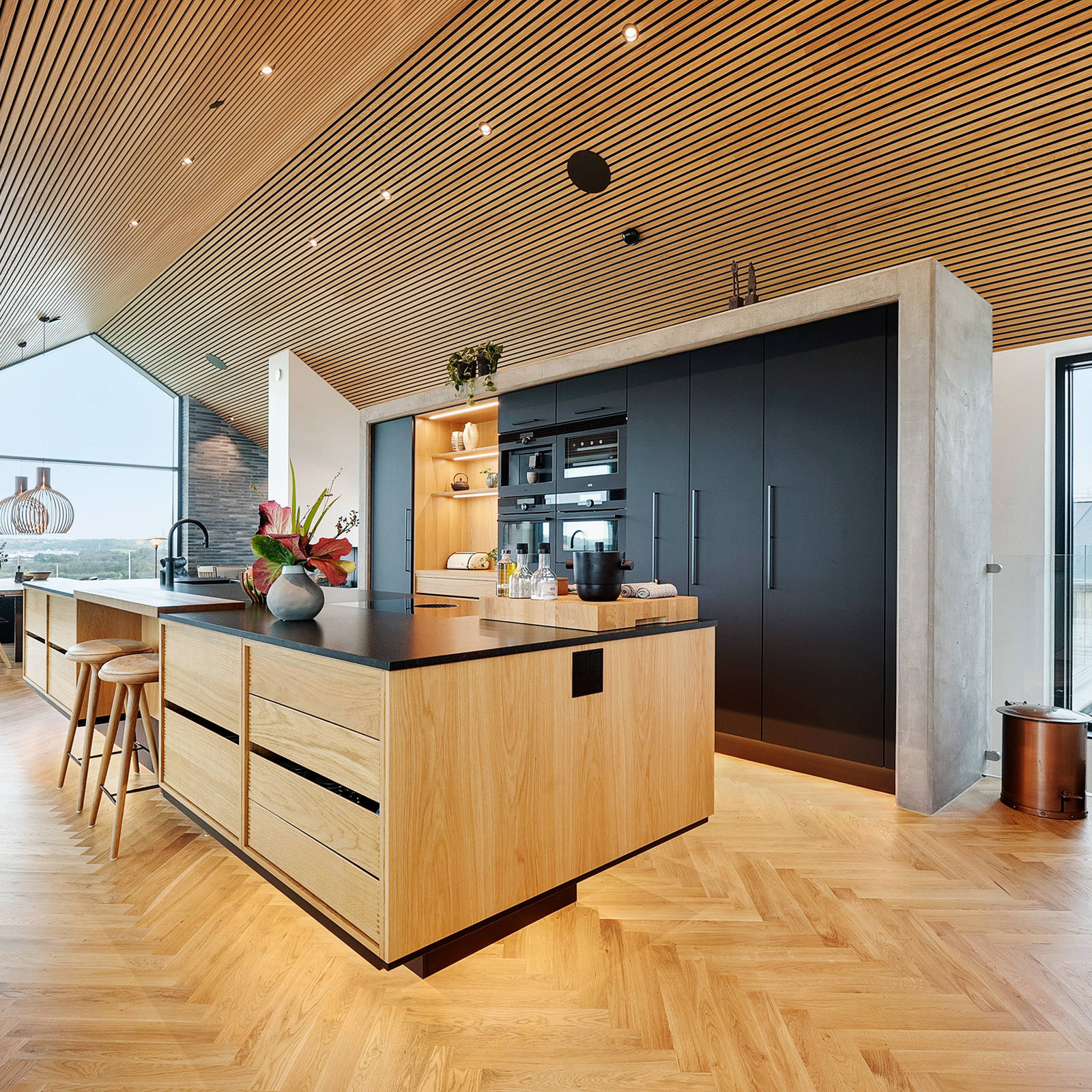 Kjøkkenøy i eik og høyskap i matt sort laminat i arkitekttegnet hus med utsikt over Limfjorden