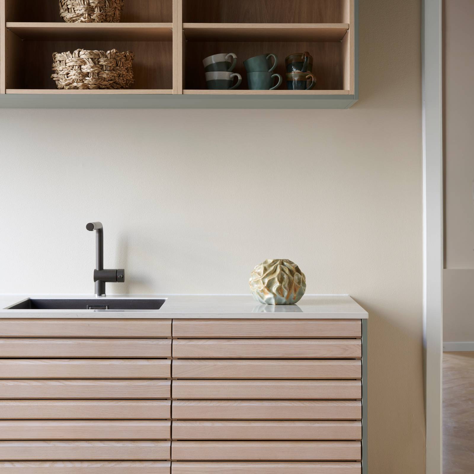 Nærbillede af egetræskøkken Ikon med håndsorterede lameller i massiv eg, kombineret med overskabe og åbne væghylder grebsfrie grønne køkkenet Highline Salvie med indfræsede greb i lågerne fra INVITA