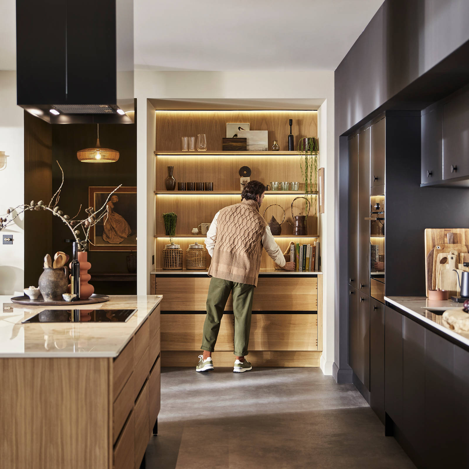Man organising reaching for cook book in natural oak open shelves with matching wall paneling over Nordic Craft cabinetry.