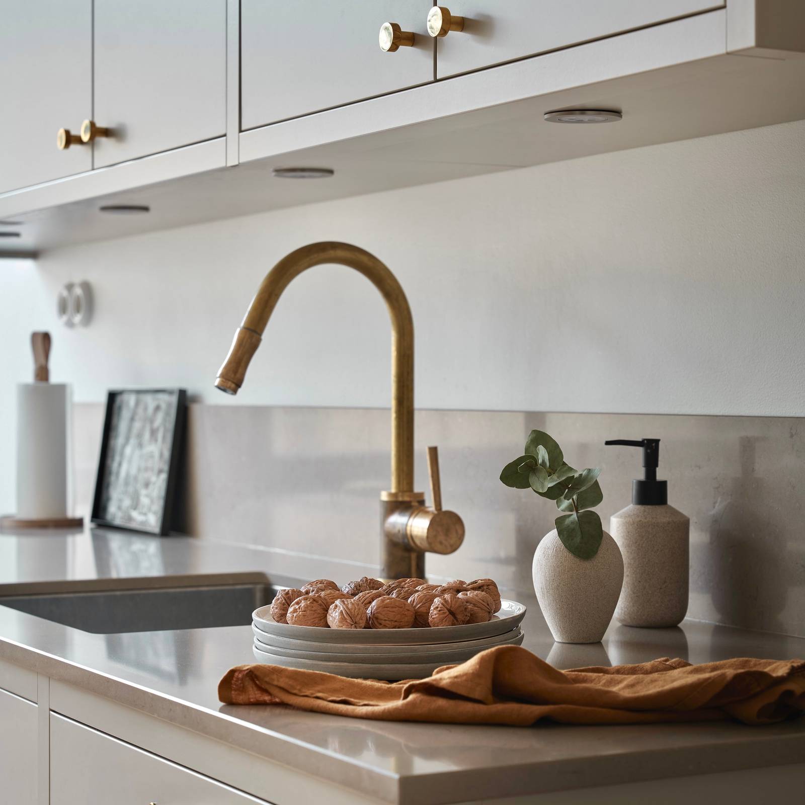 Nærbillede af messing armatur i forrammekøkken Athena Fusion i lys grå farve Sky fra INVITA med grå stein bordplade, messing håndtag