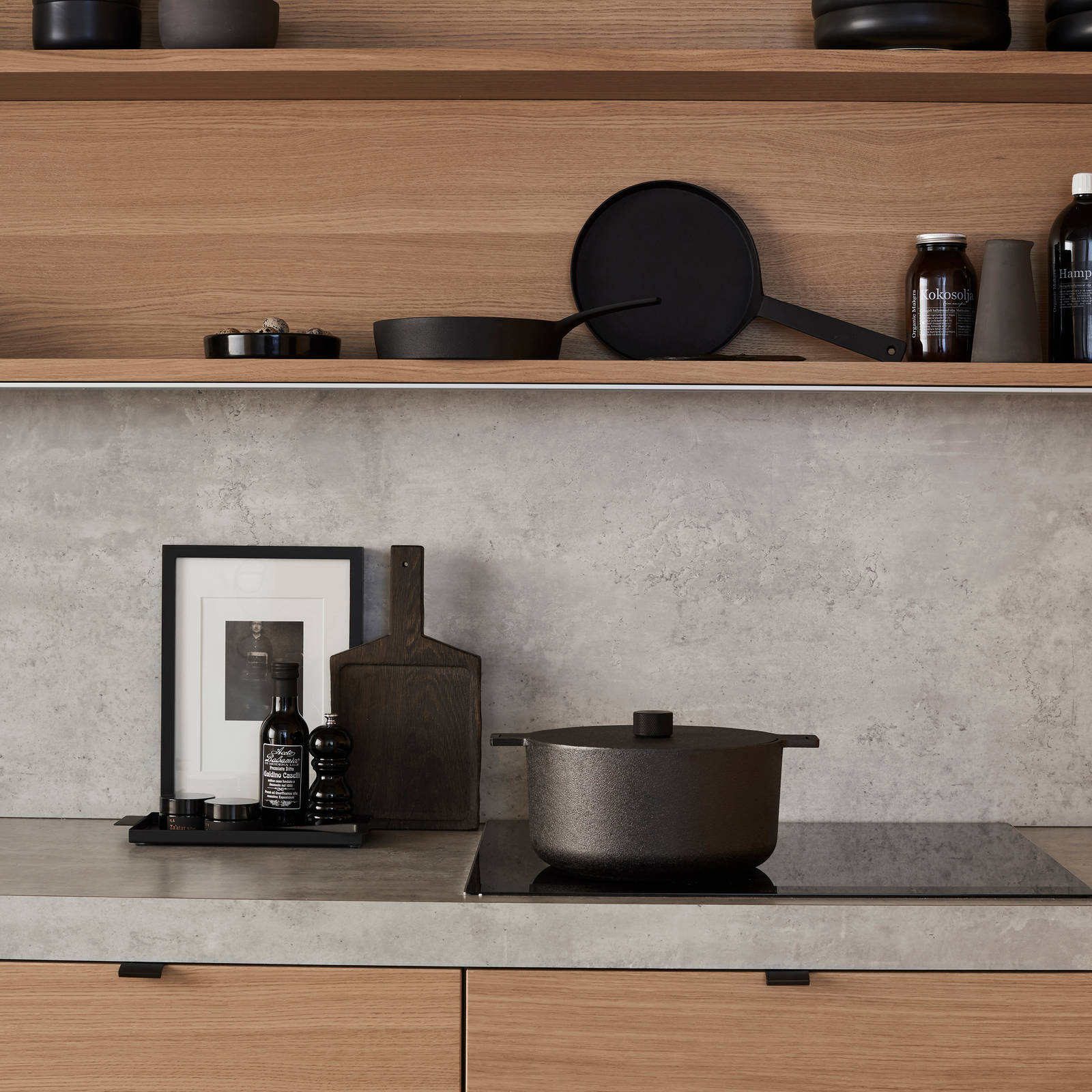 Nærbillede av finér eg natur køkken Athena fra INVITA, med matchende væghylder, laminat bordplade og splashback med betonmotiv, sort håndtag.