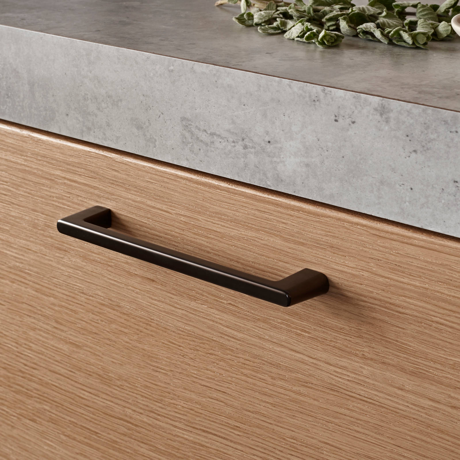 Nærbillede av finér eg natur køkken Athena fra INVITA, med laminat bordplade og splashback med betonmotiv, sort håndtag.