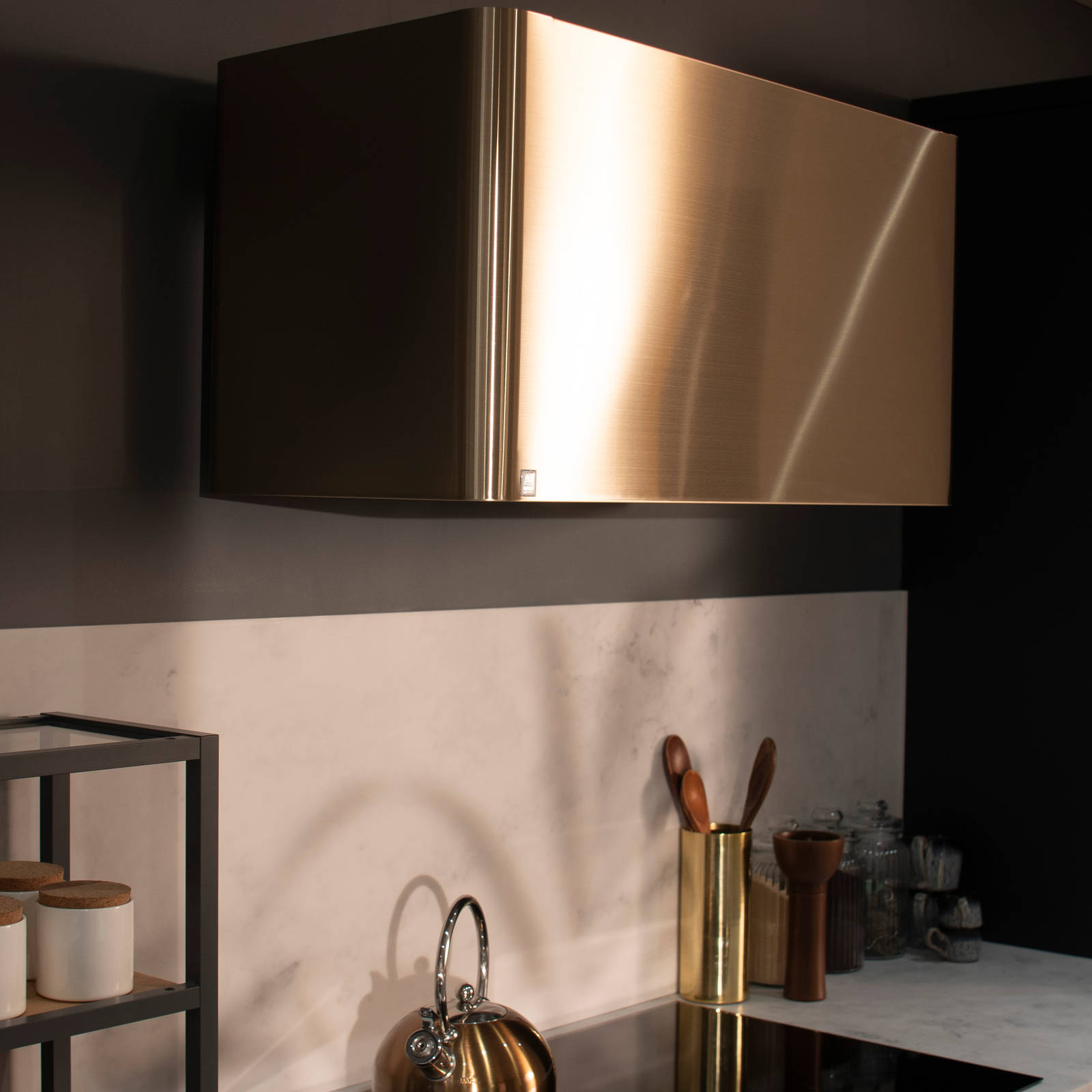 Brass hood over induction hob in a dark Luna kitchen with brass details