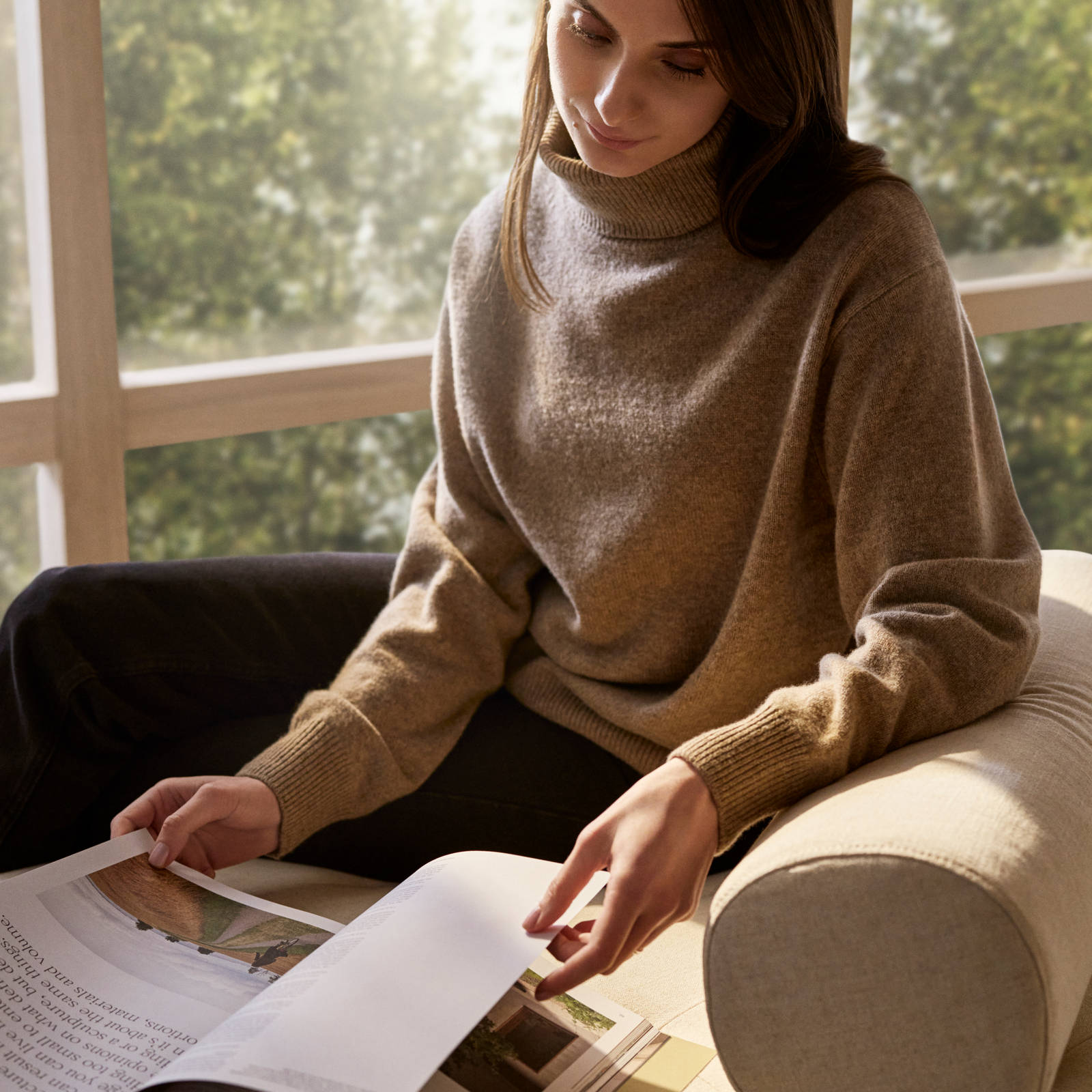 Ung kivnna i naturfärgad stickad bläddrar i en katalog på en beige soffa
