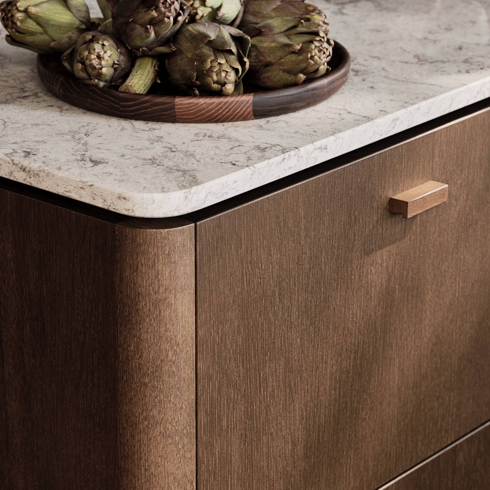 Nærbillede af afrundet hjørne på køkkenø Forever Oak fra INVITA, mørk eg køkkenskabe og håndtag med afrunded Mont Blanc Quartzite bordplade