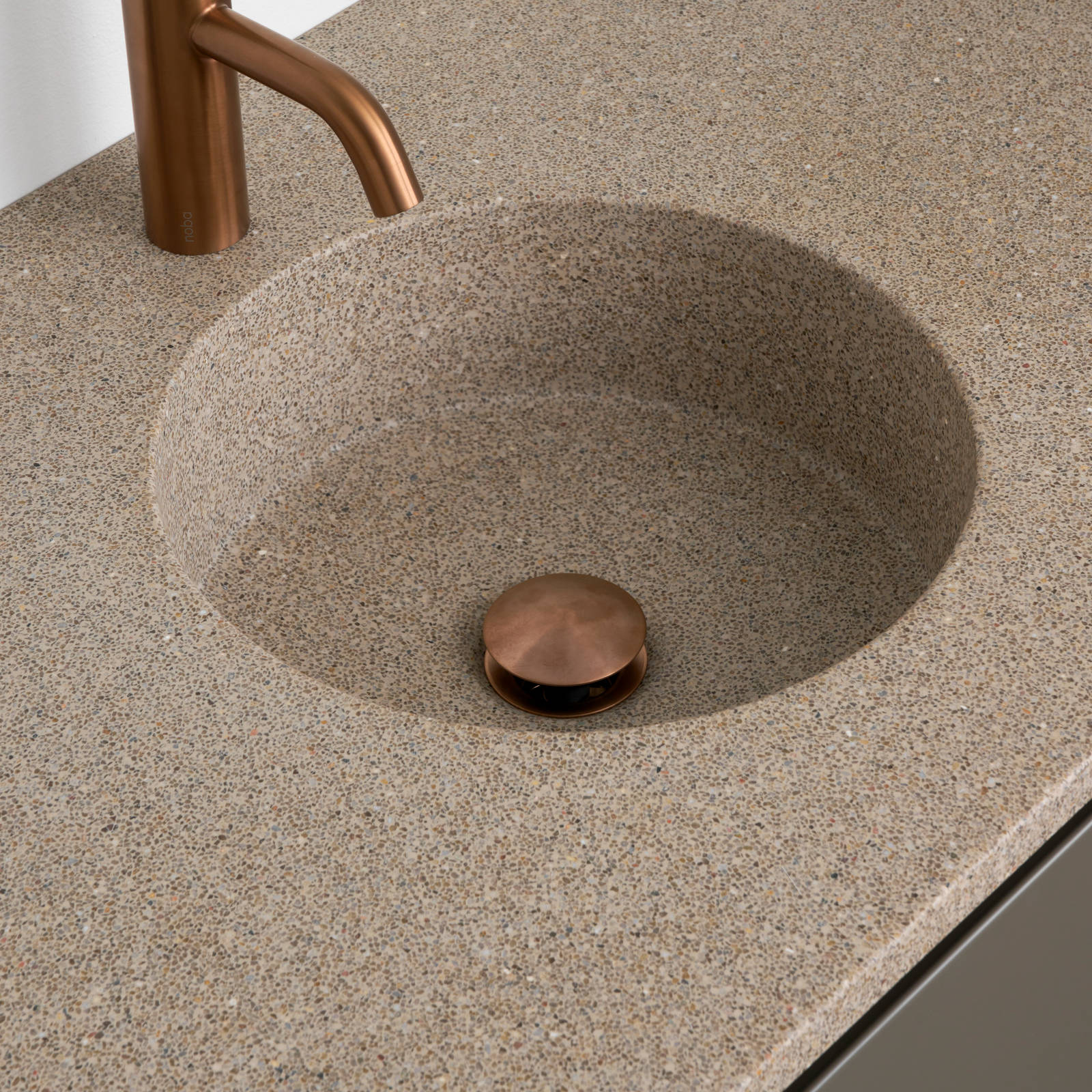 Nærbillede af bordplade stone beige 99 med vask cannes-30-30 og Cassøe borstet kobber armatur i moderne badeværelsesmøbel Urban med indfræsede greb i brune farve Bark og