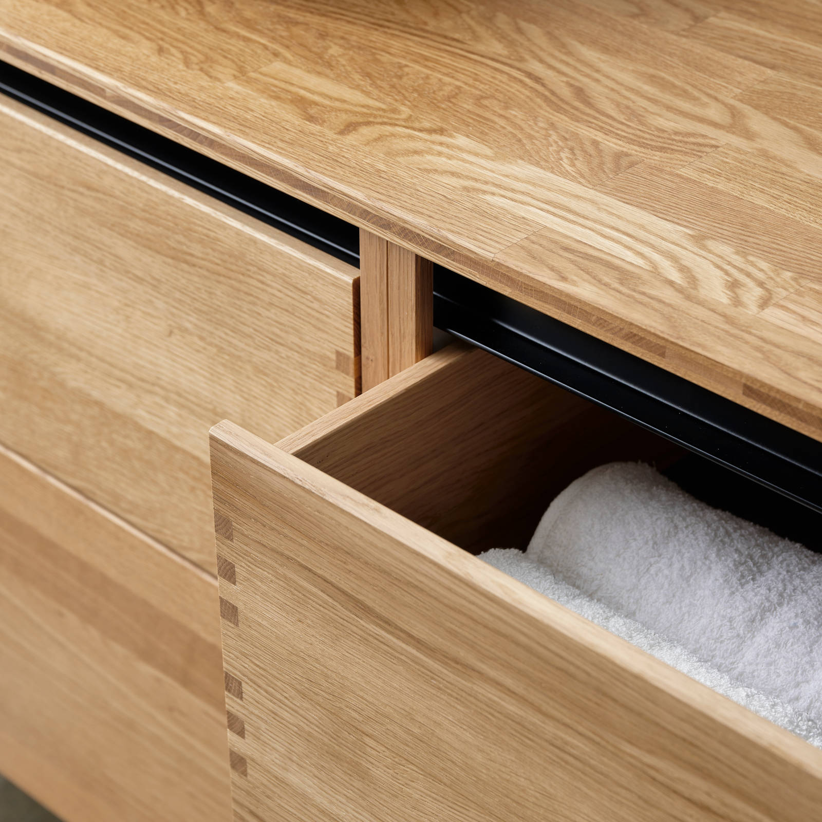Nærbillede av åben badeværelsesskuffe i massiv egetræ badeværelsesmøbel GLØD fra INVITA med fingertappede samlinger og grebsløse skuffer