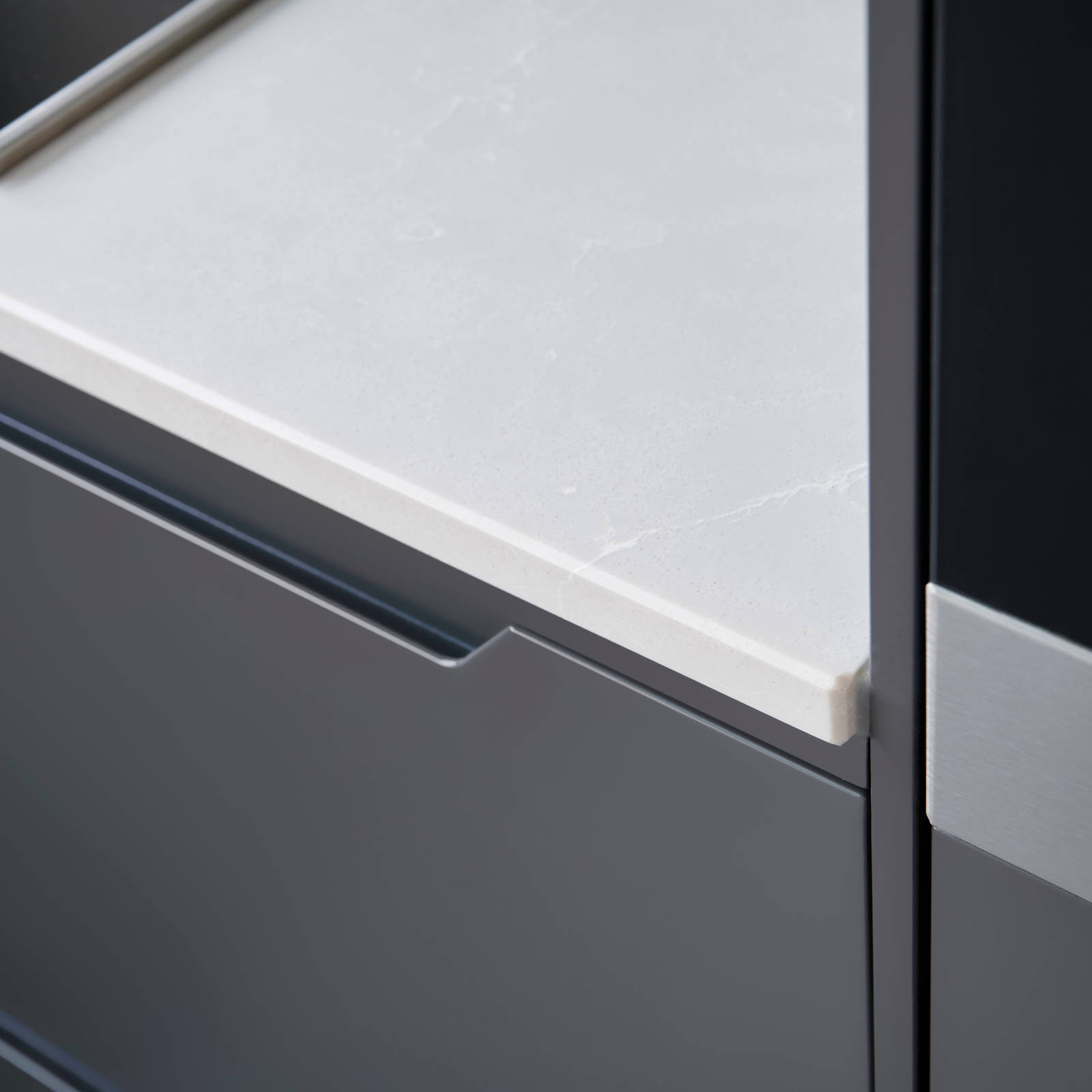 Nærbillede av hørne på mørk grå køkken Urban Granit fra INVITA med indfræsede greb og hvid bordplade
