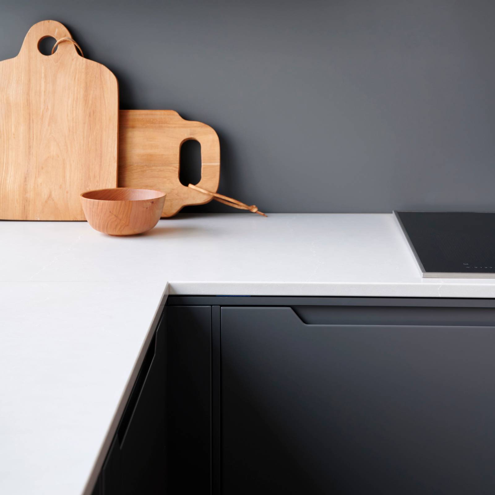 Nærbillede av hørne på mørk grå køkken Urban Granit fra INVITA med indfræsede greb og hvid bordplade med skærebrætter i træ