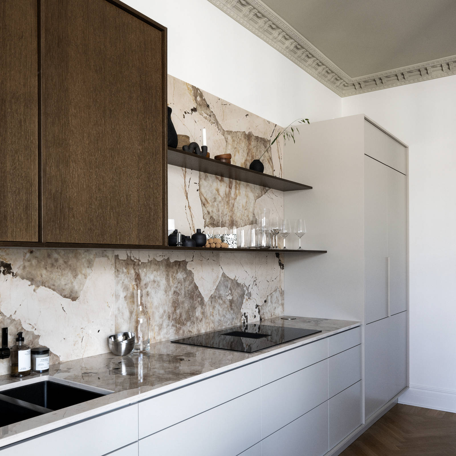 Køkken med en kombination af køkkenbænk og højskab i beige Arkitekt Plus Sand med overskab i Signatur Ekbacken fineret egetræslåge i brunbejdset fra Marbodal, bordplade og stænkplade der matcher og åbne væghylder i brunbejdset eg finer.