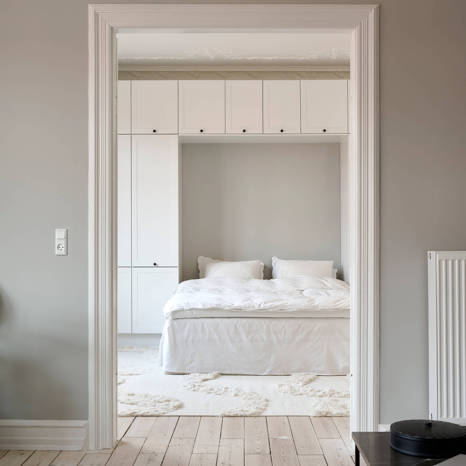 Hvid tidløs garderobe Square Sand fra INVITA omkring en seng med en kommode over, sorte greb på karmdøren