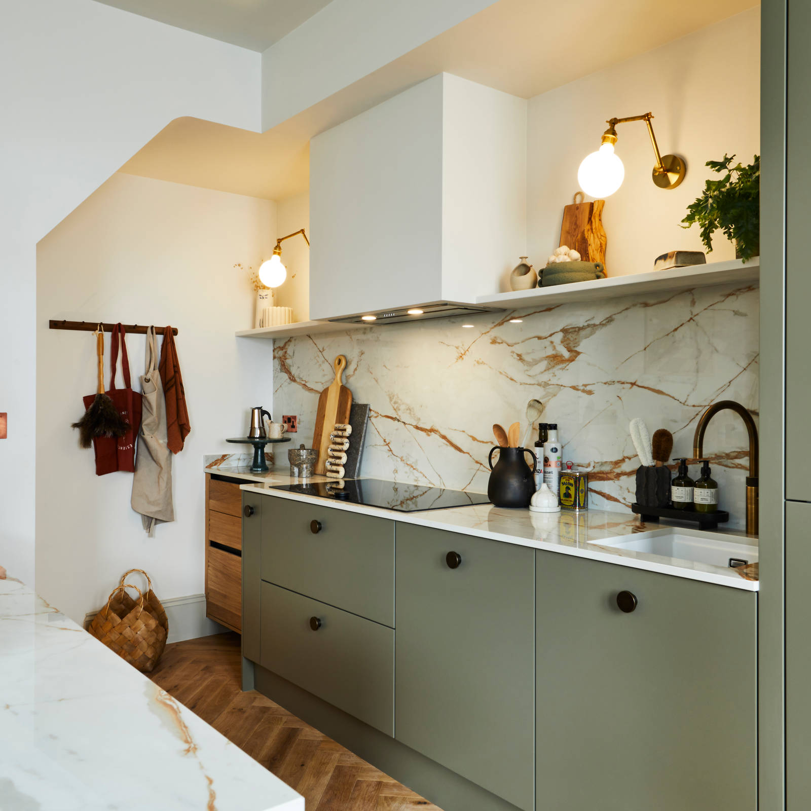 Modern slab Soho Balmoral cabinet paired with modern appliances, a marbled worktop and backsplash, brass details and plants.