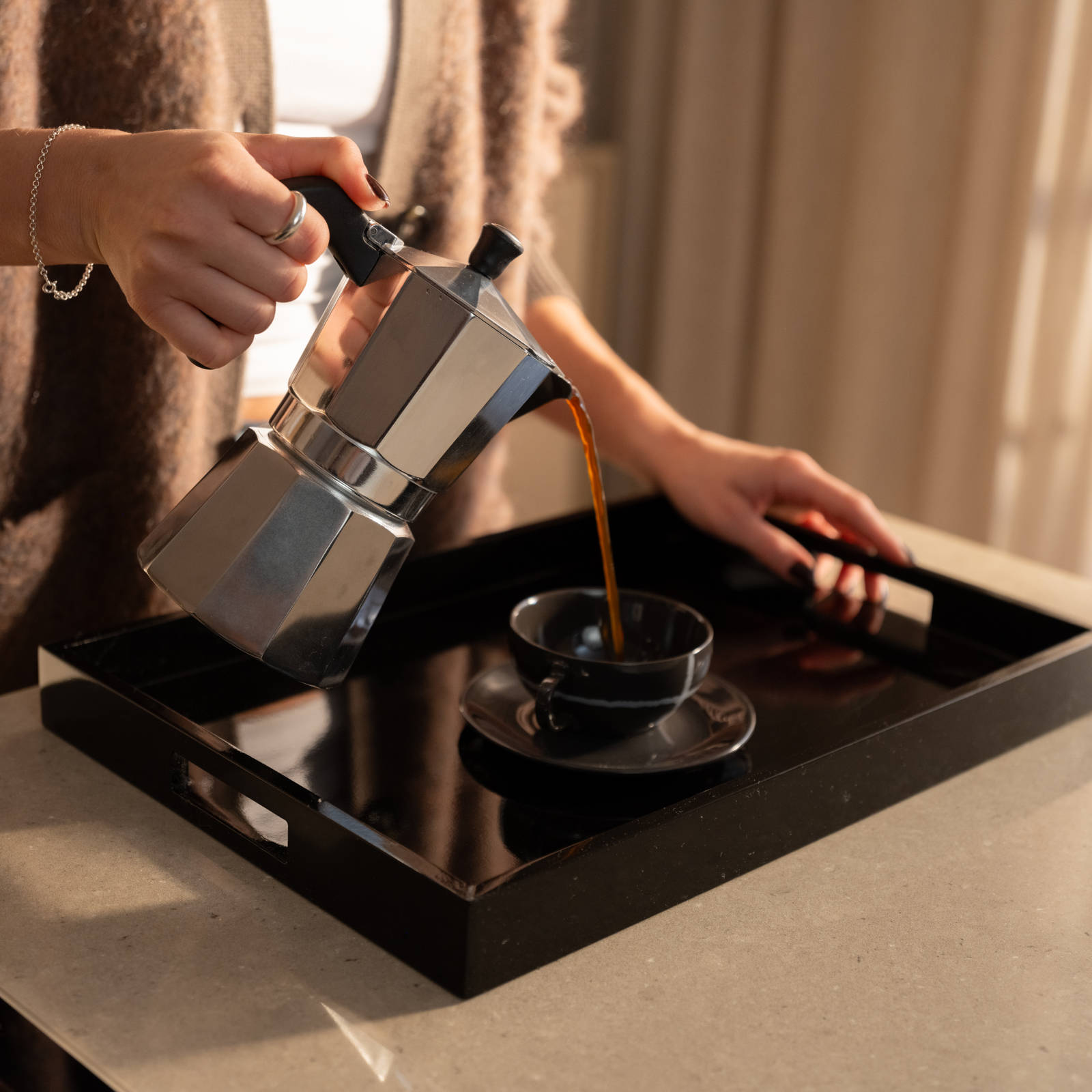 Närbild av kvinna som häller upp kaffe ur en espressokokare i kopp på en svart bricka