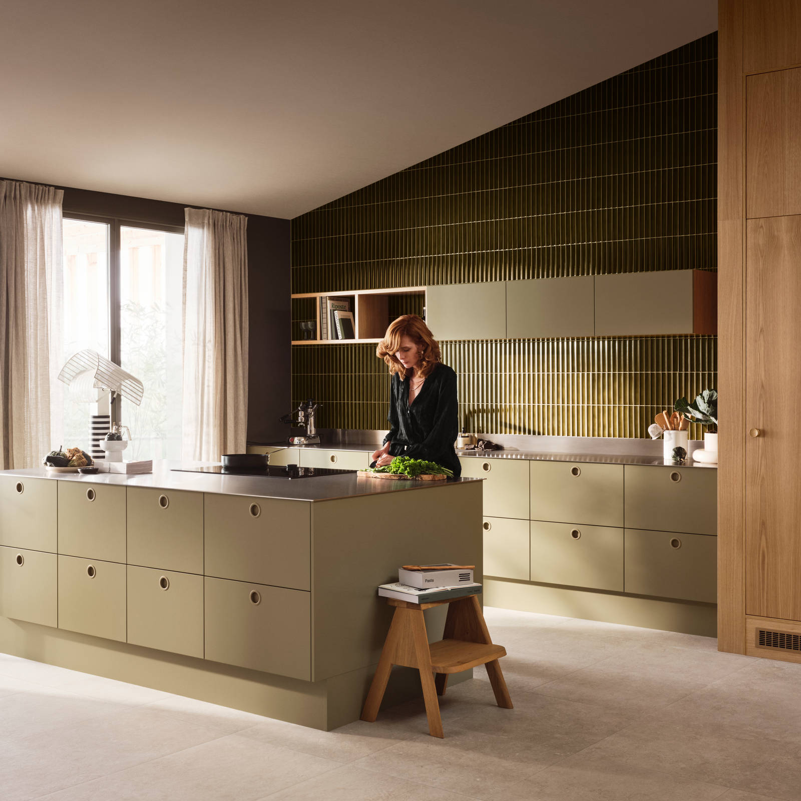 Kvinde i Jubilæumskøkken fra INVITA med træfinér eg, matchende vægpanel og grønne skaber inspireret av 1970'erne med infræsede greb