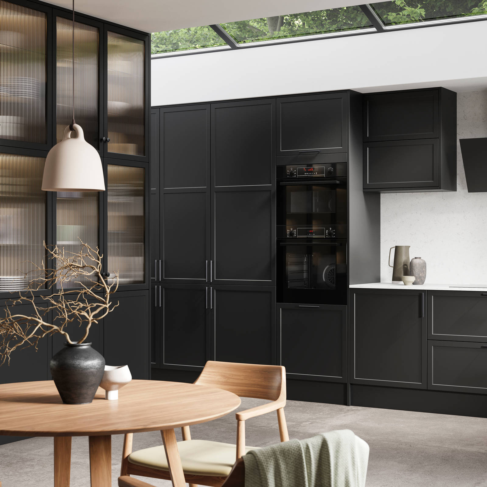 View of modern shaker kitchen Brunswick Sumi Black, with screen extractor over induction hob, tall fluted glass doorsvitrine cabinets, black frame skylights with wood dining table and chairs in foreground.