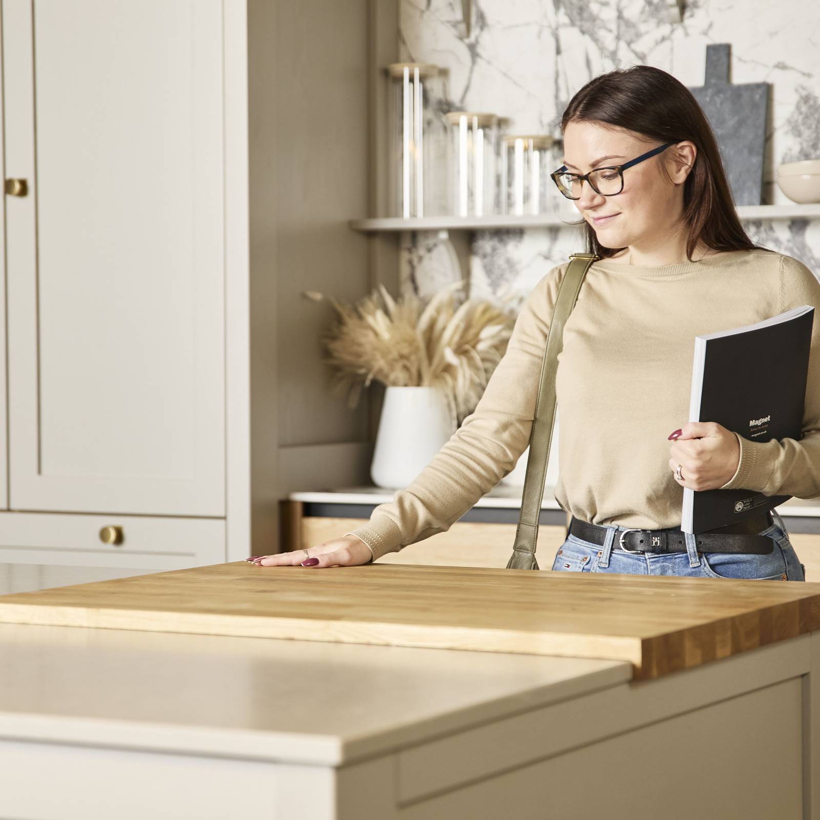 Woman holding a brochure feeling the wood worktop with her hand in a neutral shade Shaker style kitchen in a Magnet Showroom