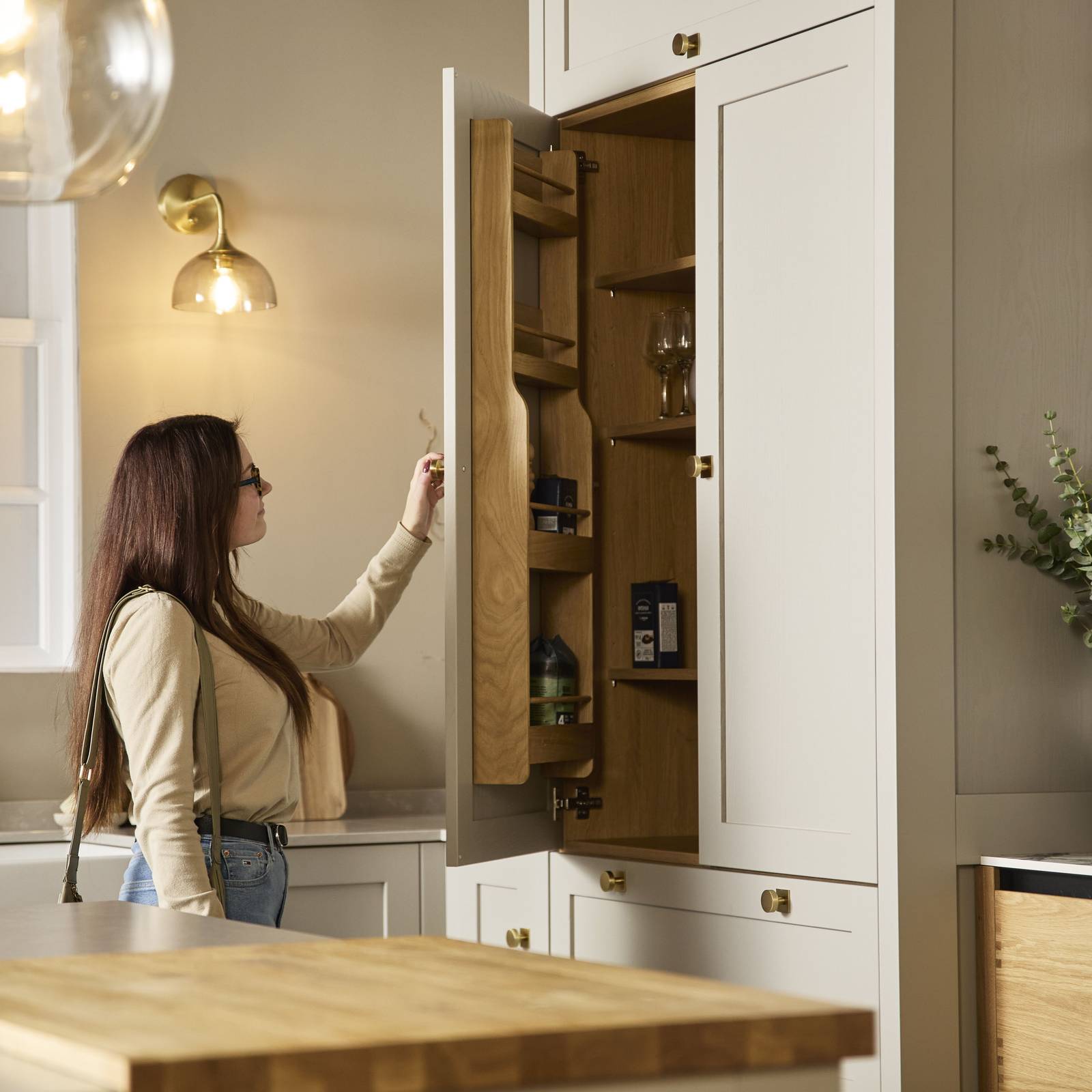 Woman in a kitchen at Magnet showroom opening larder door and looking at the oak interior.