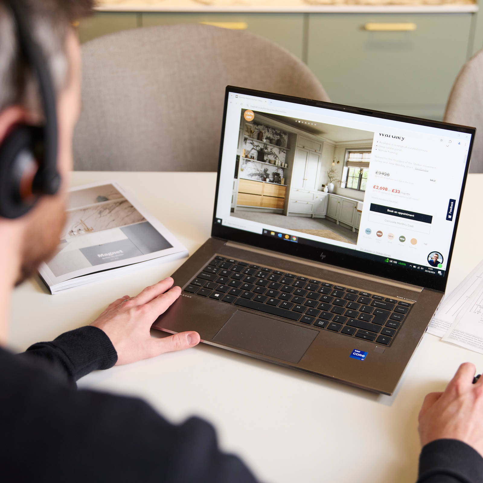 Over the shoulder view of Magnet colleague at a desk, wearing a headset browsing kitchens on a laptop computer