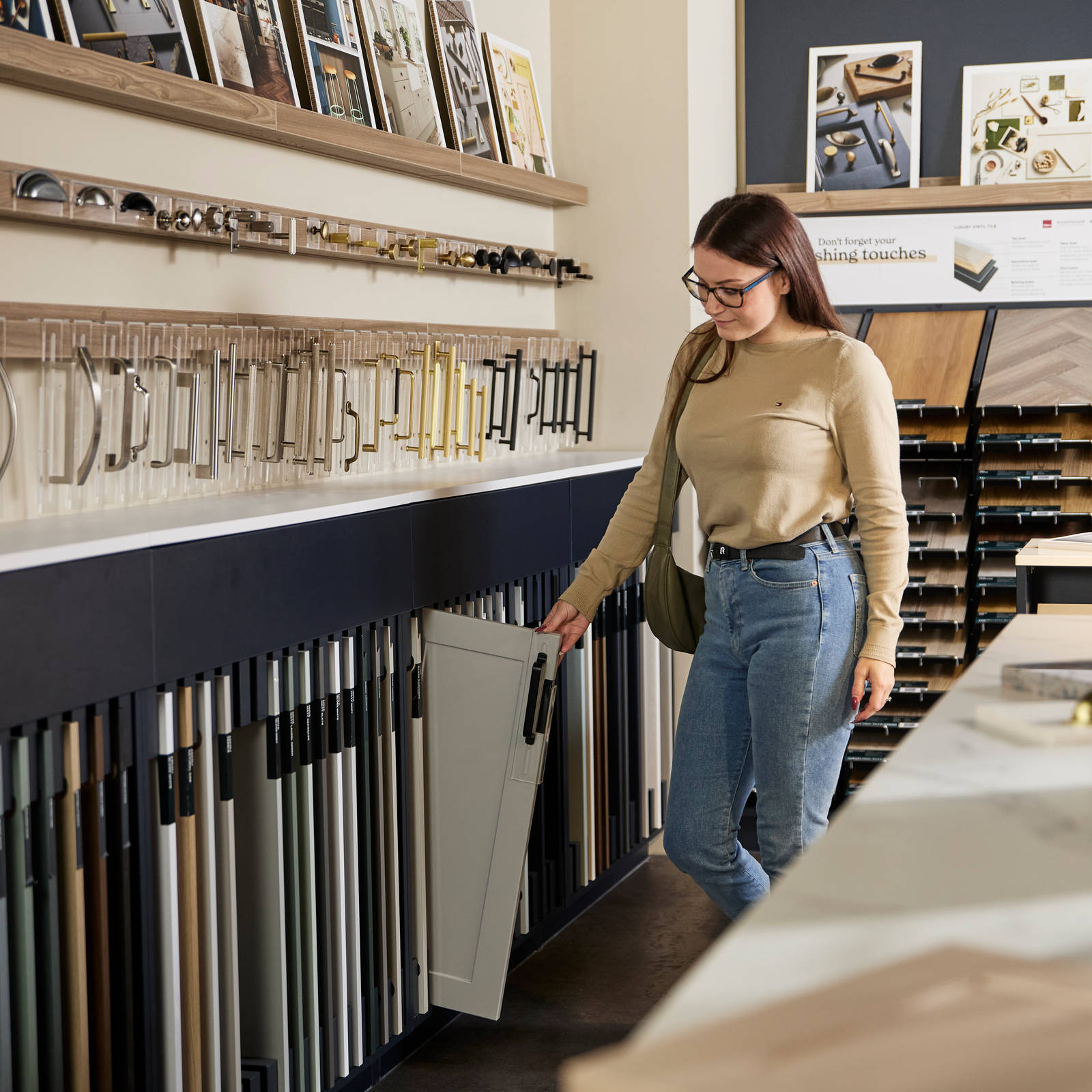 Woman pulling out a sample neutral shade Shaker front from its shelf among other samples in a Magnet Shoowroom.
