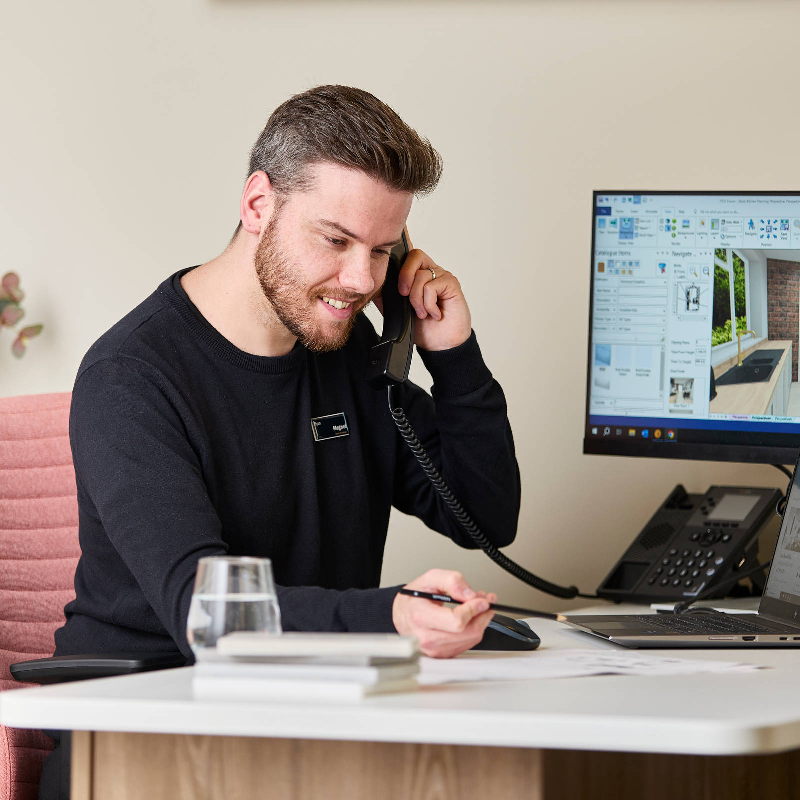 Magnet colleague at a desk, speaking on the a phone while designing a kitchen on a computer