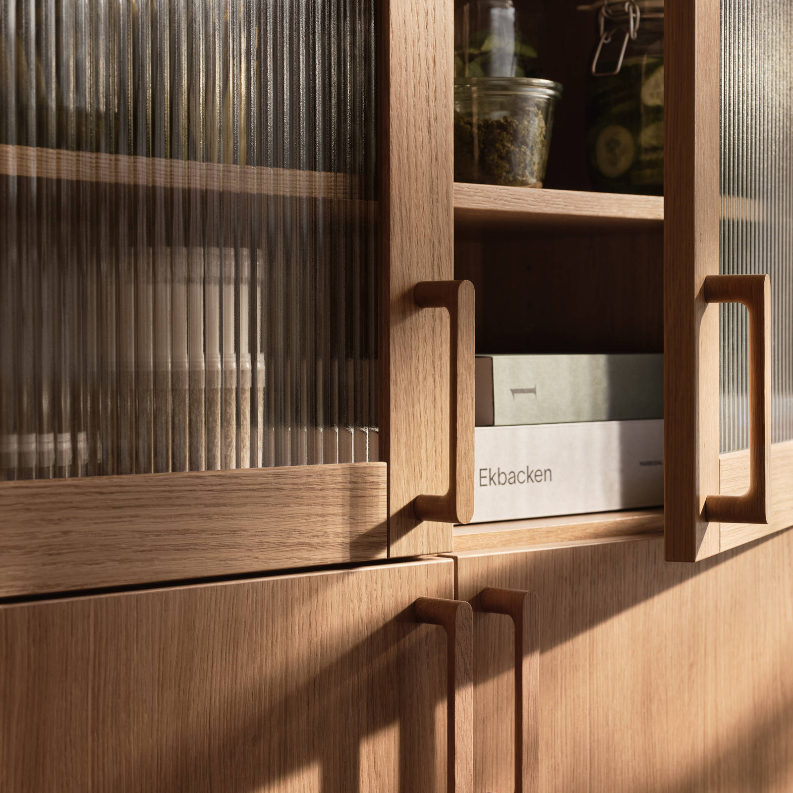 Öppnat vitrinskåp i Siri Barjes kök, räfflat glas i ram av ek, med matchande ekluckor på skåpen under och handtag i ek.