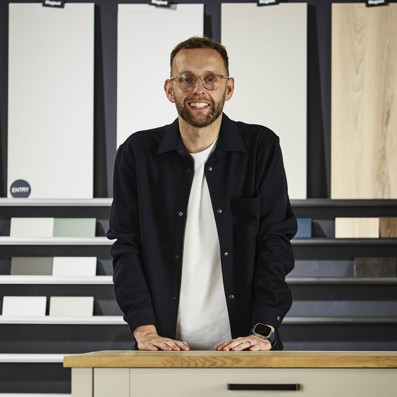 Magnet's product expert Matty Jones, pictured in our kitchen cabinet testing facility, with a range of kitchen cabinet colours and textures in the background.